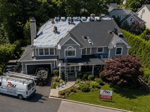 Roofers NJ crew working on the roof of a large stucco colonial home in New Jersey with branded Ford Transit van and free-estimate yard sign