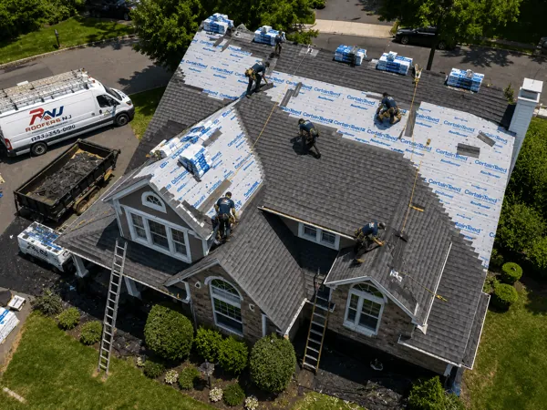 Roofers NJ crew replacing the roof on a New Jersey Cape Cod home with CertainTeed underlayment, branded van and free-estimate yard sign in front